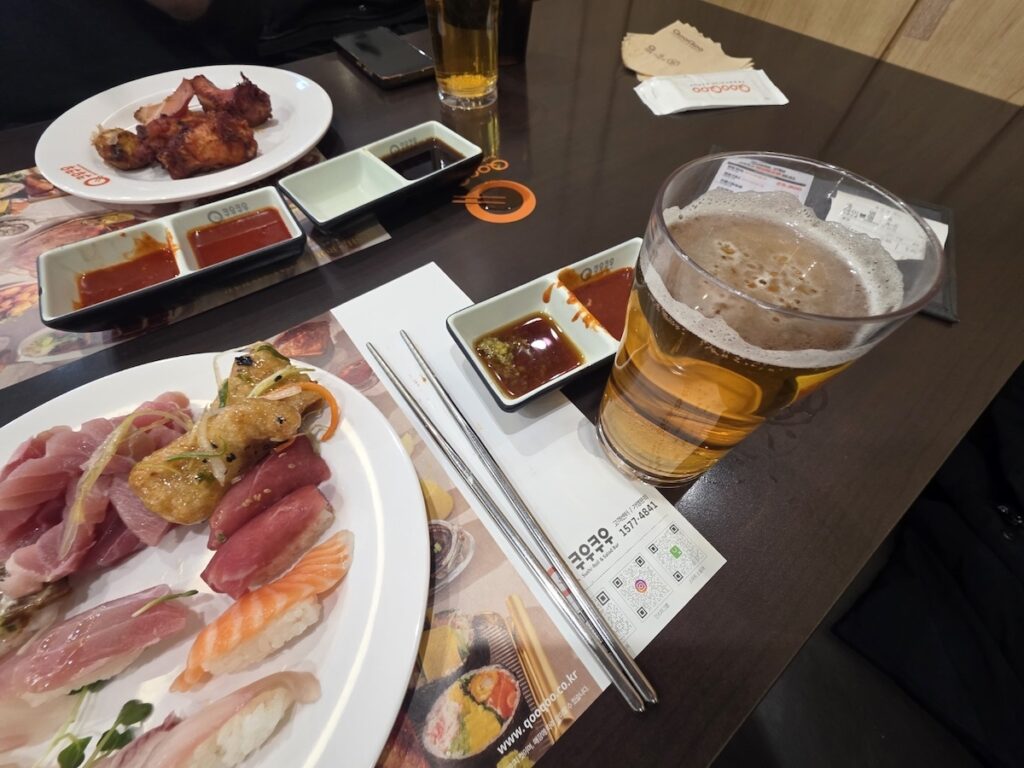 A manager holding a full plate of diverse sushi and rolls at QooQoo, illustrating the contrast and inclusive options at an affordable seafood buffet in Seoul for vegans.