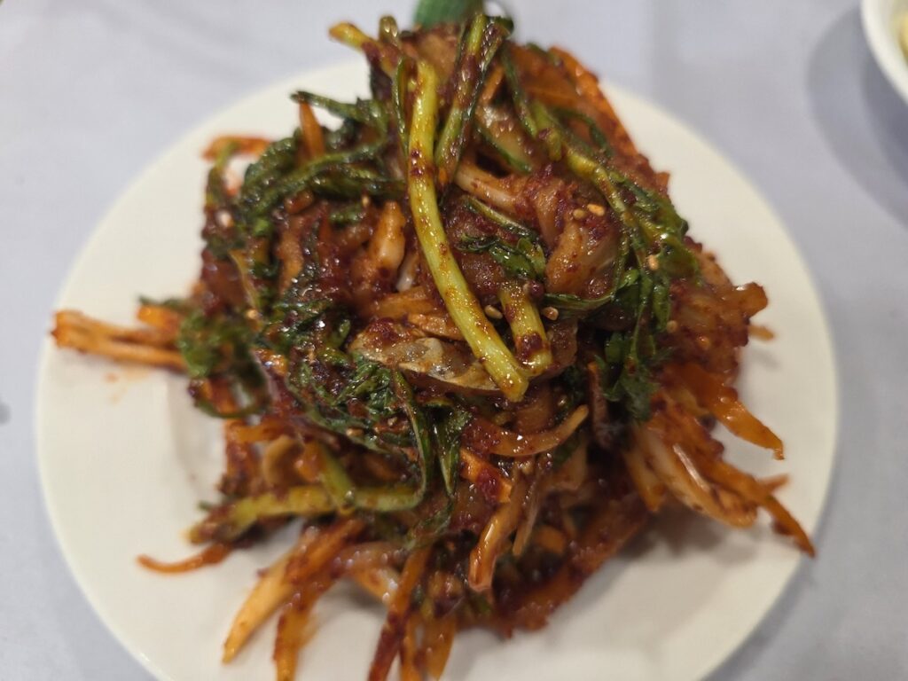 A cinematic close-up shot of authentic Korean spicy raw fish salad muchim, showing the glossy gochugaru dressing on fresh fish slices and Minari (water dropwort).