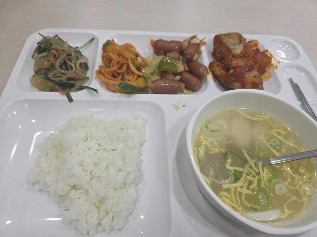 An authentic cafeteria meal for Seoul workers featuring rice cake soup and premium products from the best Korean sausage brands for office lunch rituals.