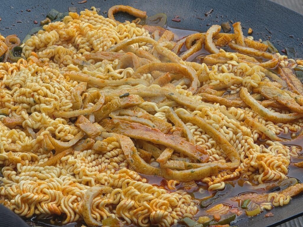 The final serving of the best Korean spicy ramen recipe with fish cakes and green onion oil, featuring a rich spicy broth and premium toppings on a cast iron griddle.