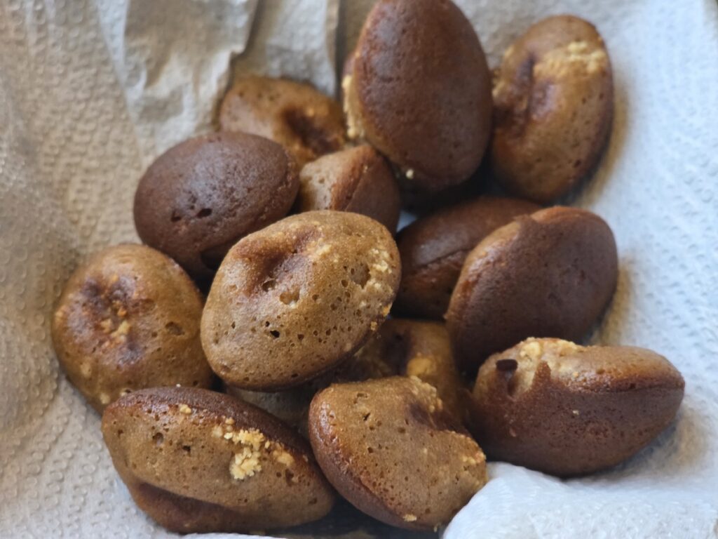 A detailed close-up shot of several freshly baked, ellipsoidal-shaped Keopi-kong-ppang (Korean coffee bean bread) pieces resting in a basket lined with paper towels, illustrating one of the 10 Trendy Coffee Bean Bread Rituals in Gangnam. The photo highlights the micro-porous texture of the crisp exterior and the golden-brown color of the pastries.