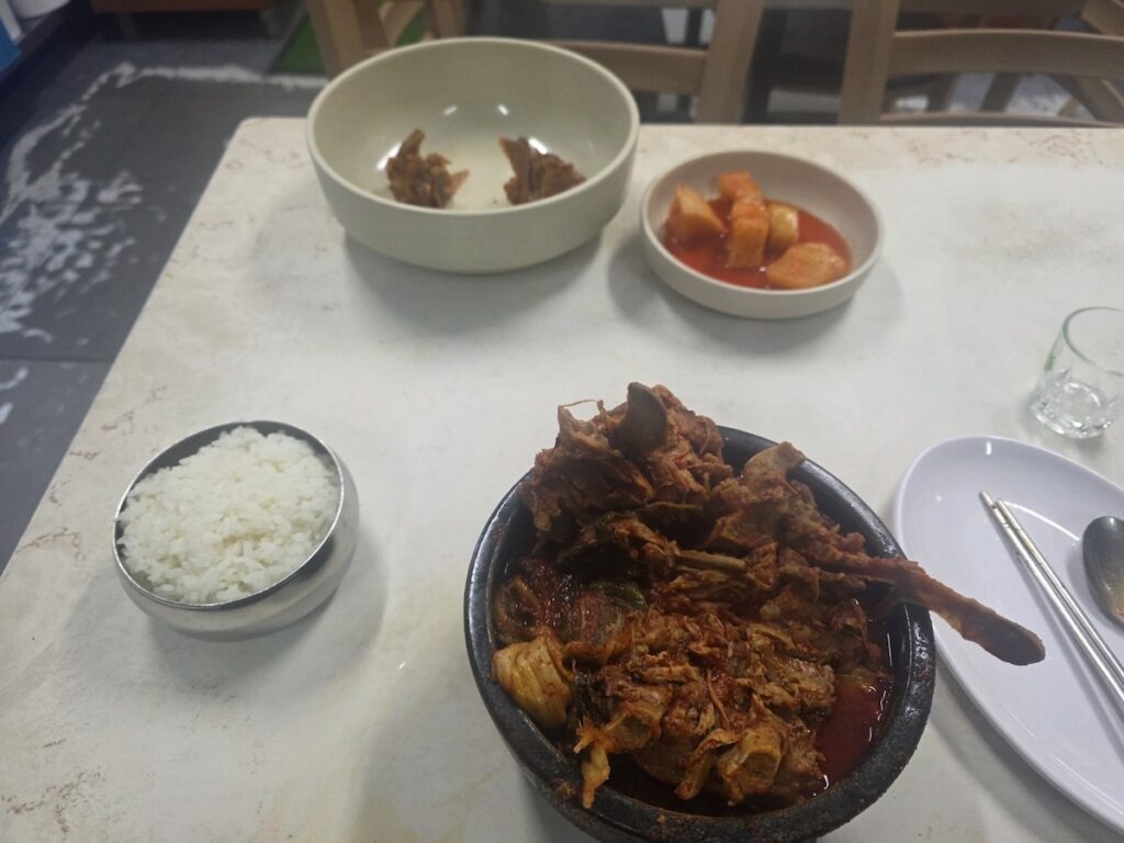 A complete table setting of the Dangerous Midnight Food in Korea, featuring the pork bone stew, rice, and radish kimchi at a 24-hour restaurant.