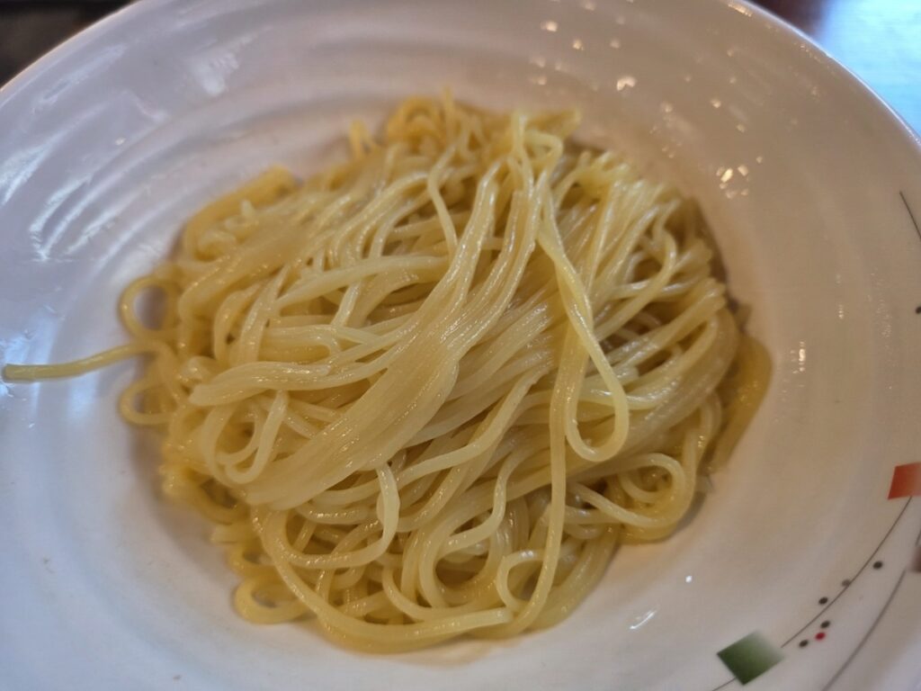 A close-up of the elastic, pale yellow noodles waiting to be mixed with the sauce for authentic Korean black bean noodles.