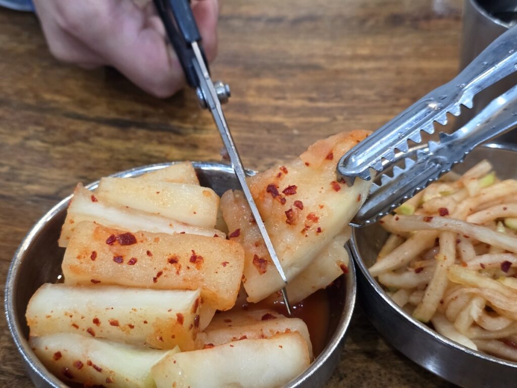 Cutting Korean radish kimchi with scissors at a Korean BBQ restaurant table