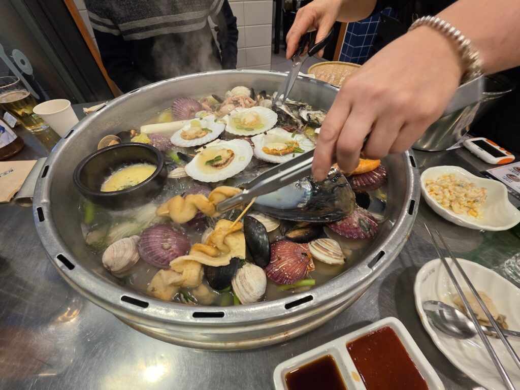 Servers preparing the 3 Best Korean Steamed Seafood Rituals for Healthier Living by cutting the seafood with tongs and scissors.