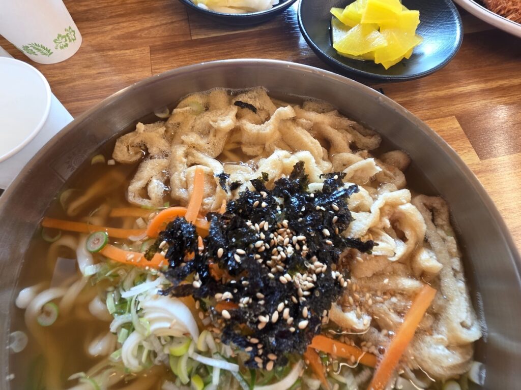 Korean Knife-cut Noodles (Kalguksu): A steaming bowl of handmade noodles served in a savory, clear broth at a local restaurant.