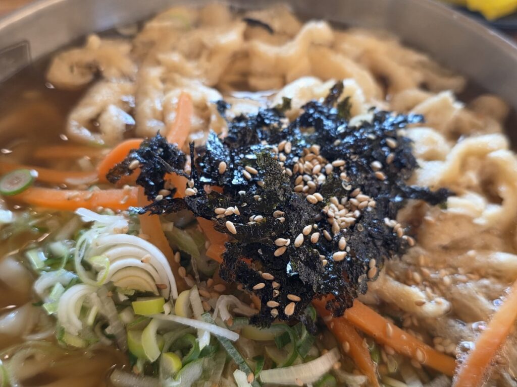 Korean Knife-cut Noodles (Kalguksu): A complete table setting showing Kalguksu served with a side of spicy Dadaegi sauce and fresh Red Kimchi for the ultimate flavor customization.