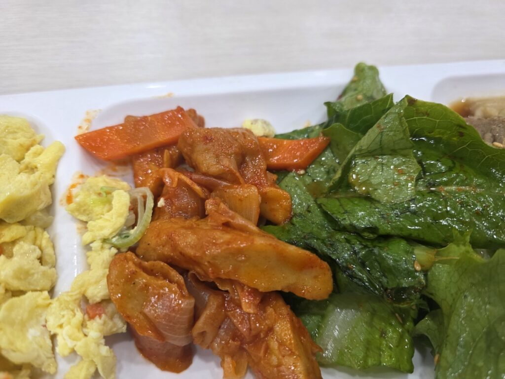 Best Korean Foods for Weight Loss illustrating the "Guilt-Driven Vegetable Ritual" with spicy pork paired with a larger portion of fresh seasoned lettuce.