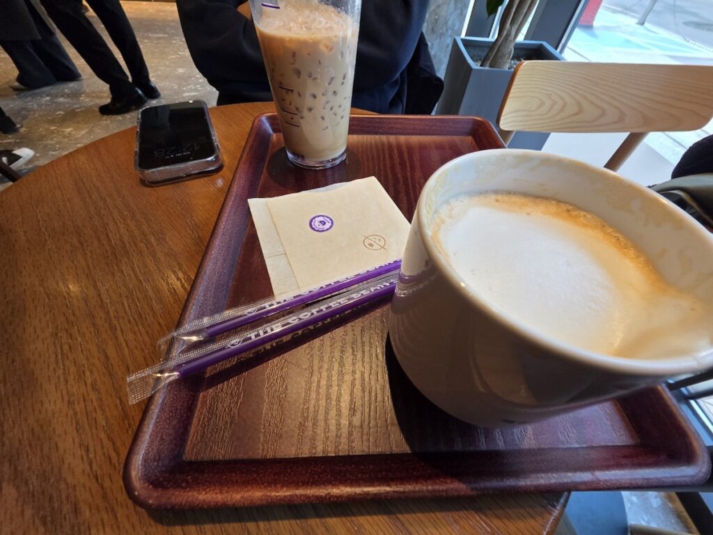 A cinematic shot of a Coffee Bean tray featuring a latte, purple straws, and a napkins with the brand logo.