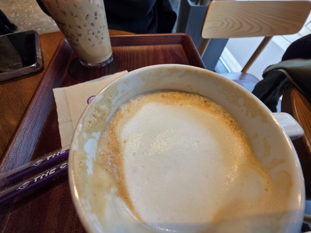 A top-down view of a creamy latte foam and the iconic purple straws at a Coffee Bean cafe in Seoul.