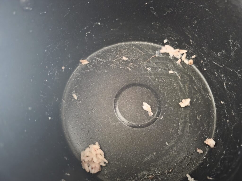 An interior view of an empty black non-stick Korean rice cooker with only a few stray grains remaining. This image captures the cultural anxiety of a depleted fuel source, highlighting why regular, 3-meal stability is the foundation of the Seoul healthy food guide.