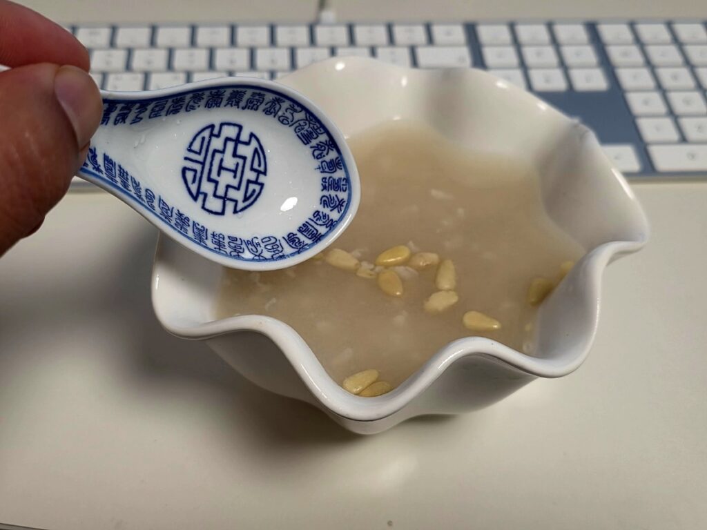 Best Korean Desserts: A rustic, elegant white ceramic bowl filled with completed home-made Sikhye, garnished with floating pine nuts and jujube flower slices, illustrating the final sophisticated presentation.