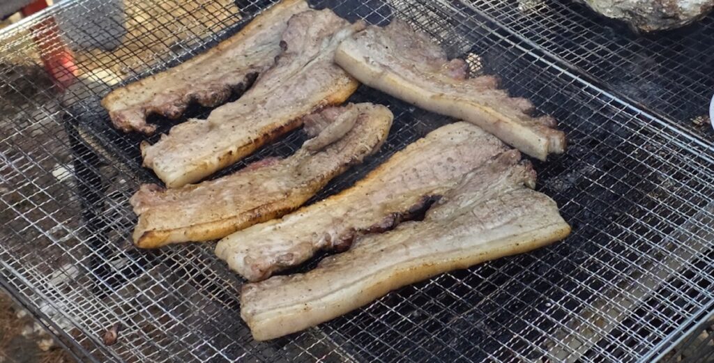 Thick slices of Samgyeopsal grilling over a charcoal fire, illustrating the sizzling anatomy of the **Korean BBQ Pork Cuts Guide 2026**.