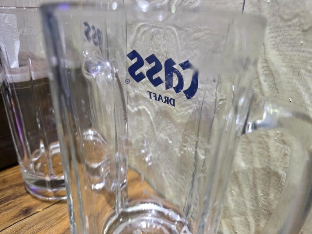 The Korea Beer Dilemma: An empty, chilled 500cc Cass Draft beer mug rests on a wooden table, symbolizing the standard after-work ritual in Seoul.