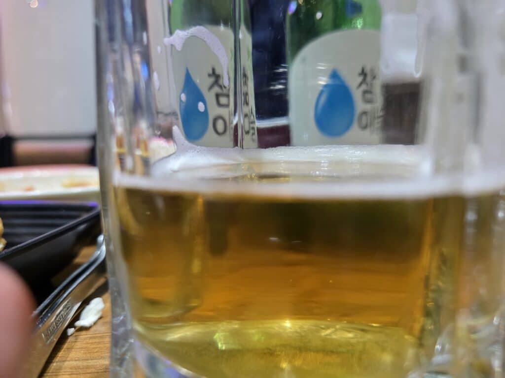 A shallow depth-of-field shot of a beer glass with Soju bottles in the background, showcasing the layered complexity of Korean drinking rituals.