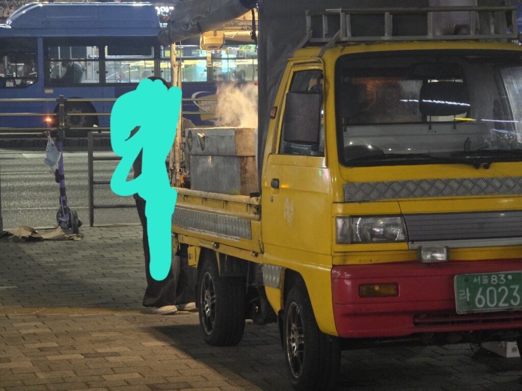 A yellow food truck with rising steam from a large metal cooker on a Friday night, showcasing the professional hygiene of the Korea Street Food Guide 2026.