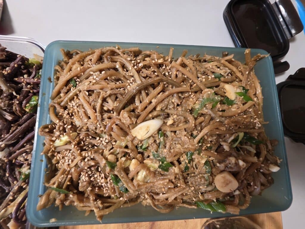 A large container of savory stir-fried sweet potato stems (Goguma-julgi bokkeum) topped with sesame seeds, representing the high-volume and healthy Korean Banchan Diet Rituals.