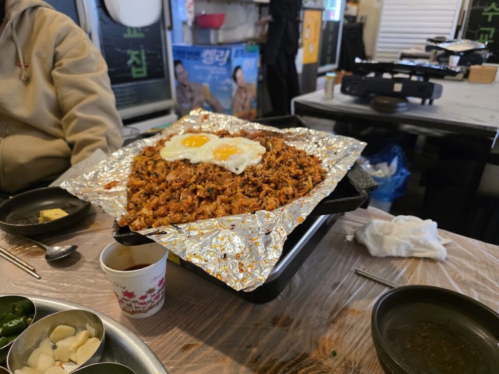 A wide shot of a traditional Korean restaurant table where a snack has been elevated to a "proper meal" through the act of frying rice in residual pork fat.