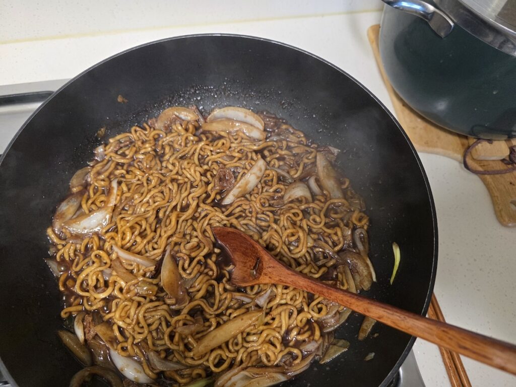 Cooking Chapagetti with onions in a pan to show the personalized Sunday Chef ritual in Korean Food Rituals 2026.
