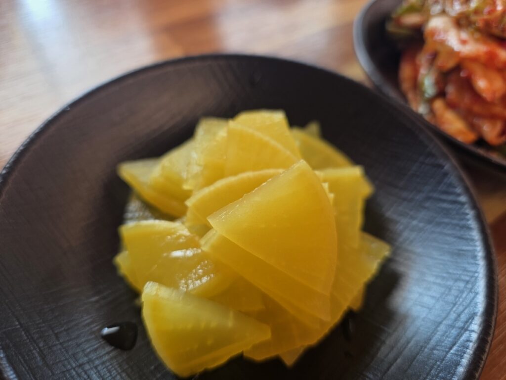 Korean Knife-cut Noodles (Kalguksu): A plate of bright yellow pickled radish (Danmuji), a sweet and crunchy side dish that cleanses the palate.