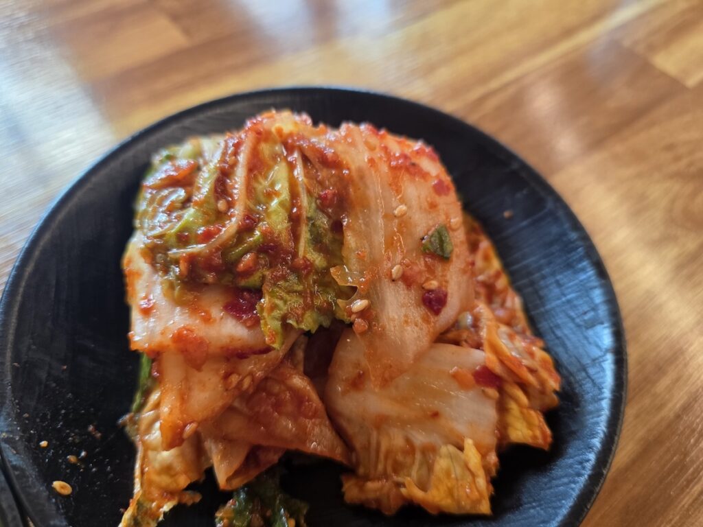 Korean Knife-cut Noodles (Kalguksu): Fresh Red Kimchi (Geotjeori), the fated partner that adds essential spice and aesthetic contrast to the white noodles.