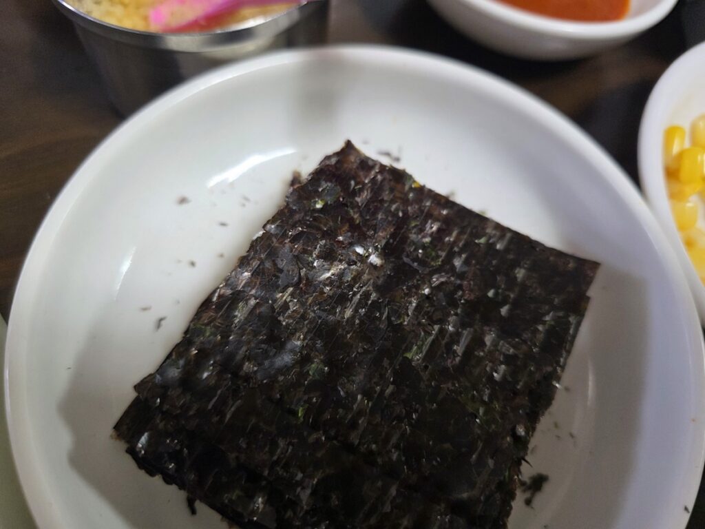 Korean Raw Fish Ssam Ritual: A close-up of high-quality dried seaweed (Gim) on a white plate, used to add a salty crunch and oceanic depth to a personalized fish wrap.