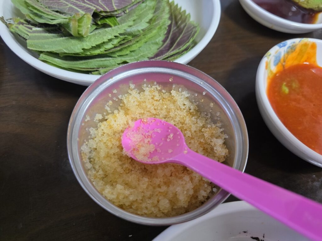 Korean Raw Fish Ssam Ritual: A vibrant bowl of flying fish roe (Tobiko) served with a small pink spoon, a key texture element used for advanced layering in a Seoul restaurant.