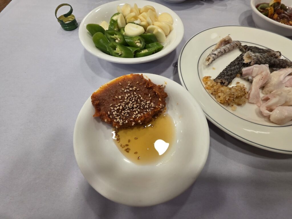 Korean Raw Fish Ssam Ritual: A close-up of a rustic Korean Ssamjang paste, seasoned with roasted sesame seeds and a velvety pool of golden sesame oil for maximum umami.
