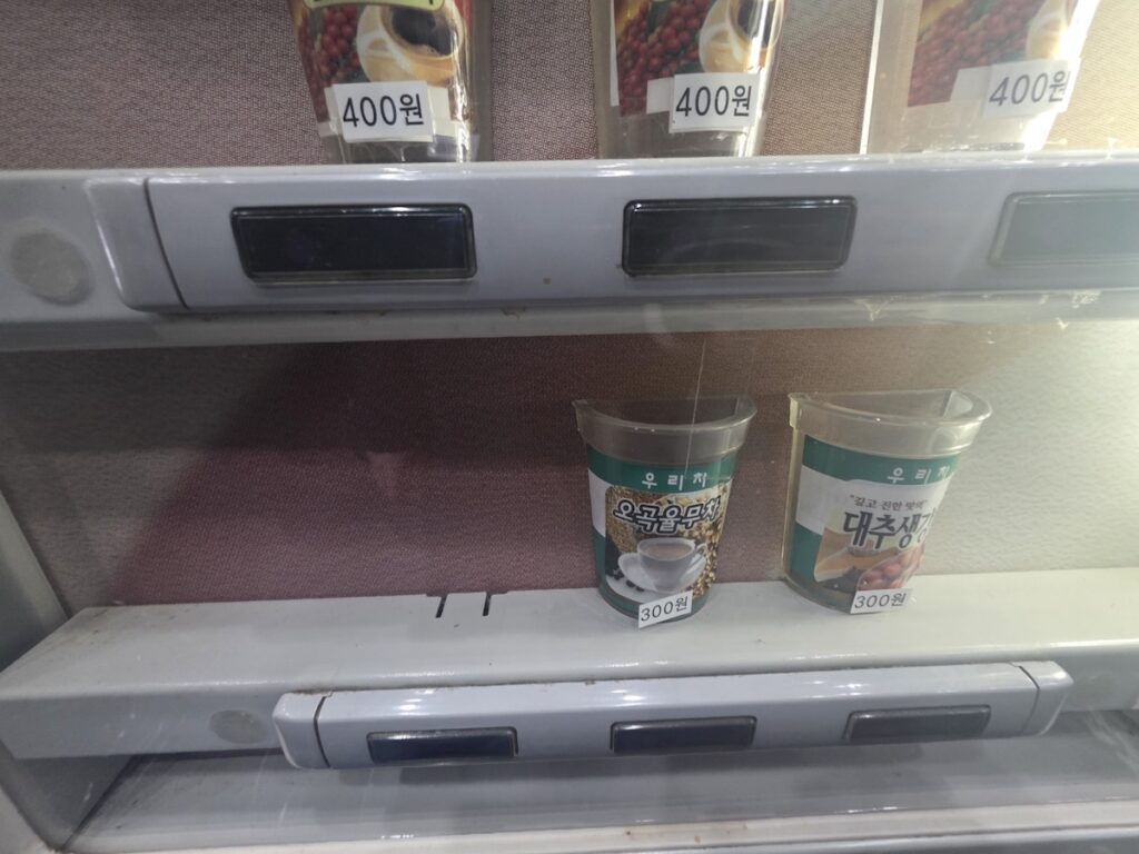 Close-up of a Korean vending machine menu showing Yulmu-cha and Daechu-saenggang-cha priced at 300 won.