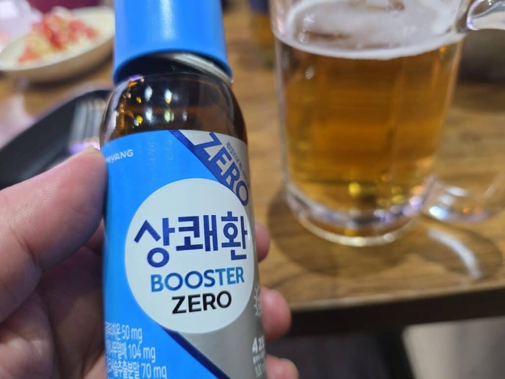 A high-resolution macro shot of the detailed nutritional facts on the back label of a 'Sang-kwae-hwan Booster Zero' (상쾌환 부스터 제로) hangover drink bottle, priced at 5,000 KRW, specifically focusing on the inclusion of Taurine to clear brain fog and restore stamina.