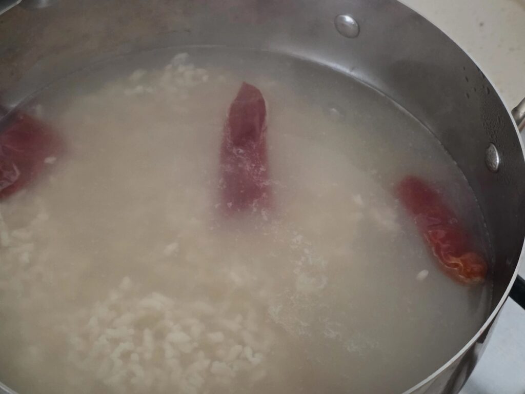 Best Korean Desserts: A close-up view of the simmering pot, focusing on the soft fermented rice grains and a whole dried red chili pepper, showcasing the family's healing brew.