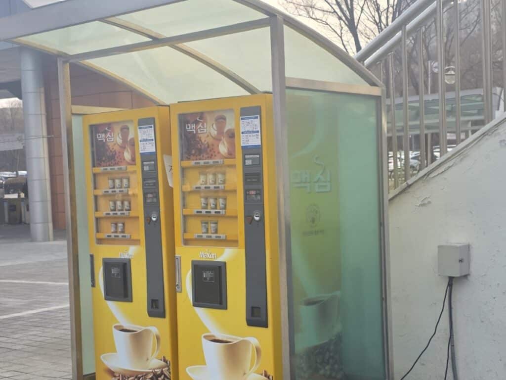 Two traditional yellow Maxim coffee vending machines standing outdoors in Seoul, a symbol of Korean street coffee culture.