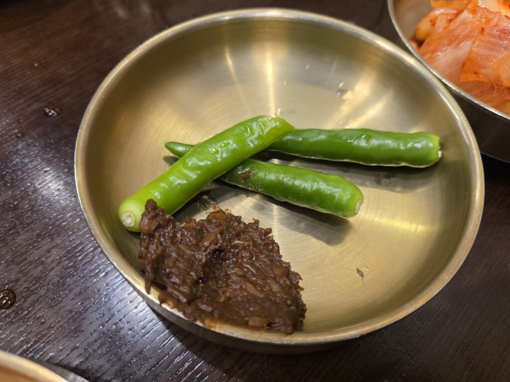 Fresh green chili peppers served with traditional fermented soybean paste (Doenjang) in a brass dish.