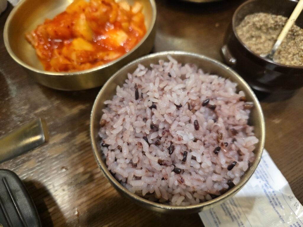 A bowl of healthy Korean purple rice (Heungmi-bap) served alongside radish kimchi in a traditional brass bowl.