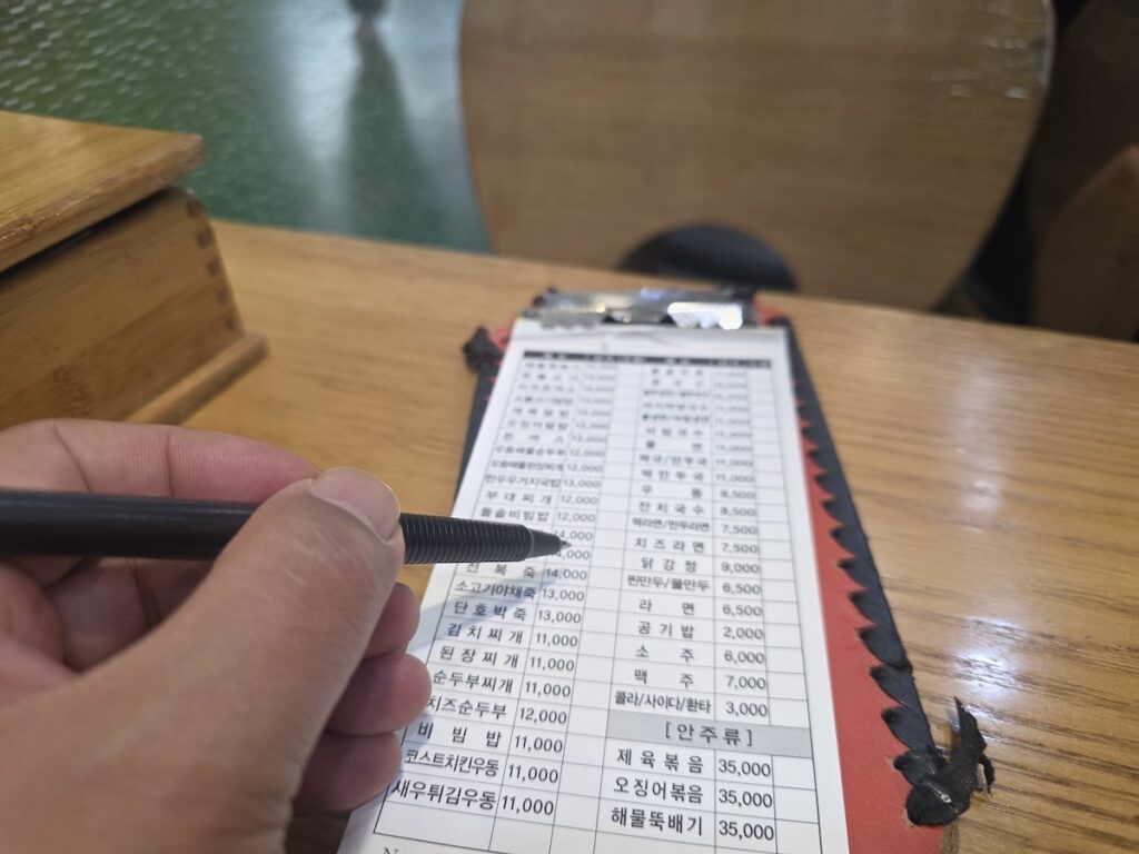 A traveler’s hand reaching to open a wooden chopstick box on a table at a cramped terminal snack bar, illustrating the complete self-service and lack of hospitality often found in transit hubs.