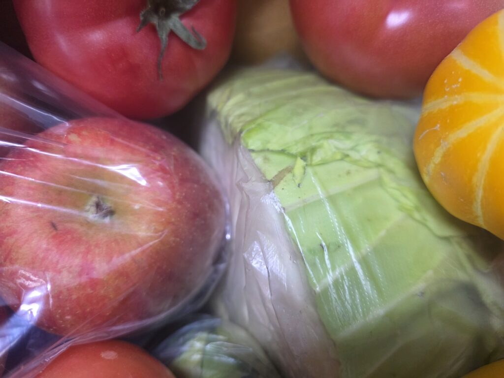 A close-up view of fresh produce including red tomatoes, a crisp green cabbage, and a yellow melon, representing the raw ingredients of a healthy Korean vegan diet.
