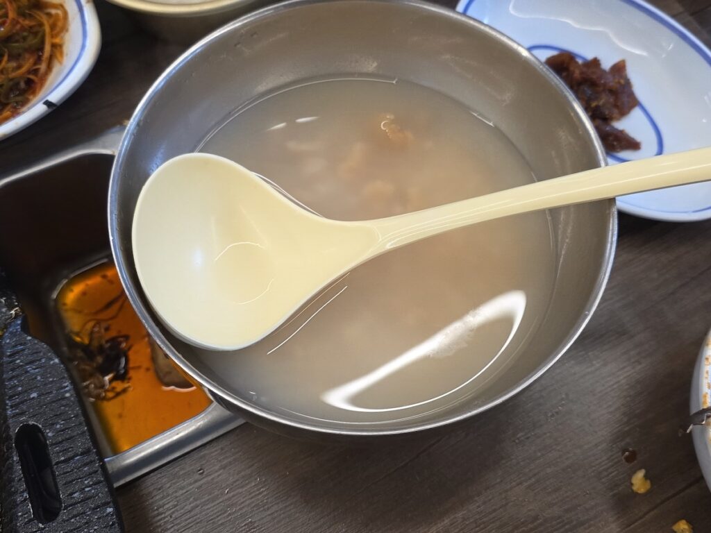 A large stainless steel bowl filled with warm rice water and scorched rice (Sungnyung), a classic choice for an after-meat meal in Korea to cleanse the palate.
