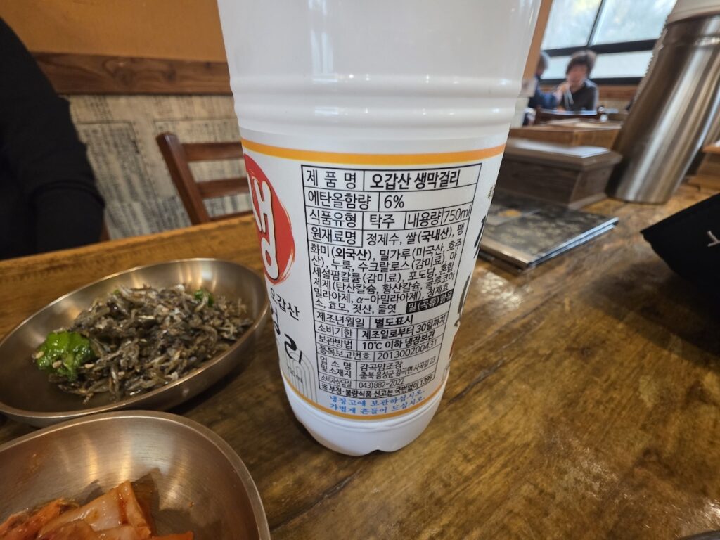 A detailed view of the back label of Ogapsan Saeng Makgeolli, showing ingredients like domestic rice and 6% alcohol content, featured in a Regional Makgeolli Guide.