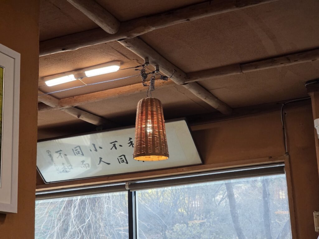 The ceiling of a traditional Korean restaurant, featuring unique light fixtures covered in dried rice straw and a large, horizontally hung calligraphic banner with Sino-Korean characters on a wooden beam.