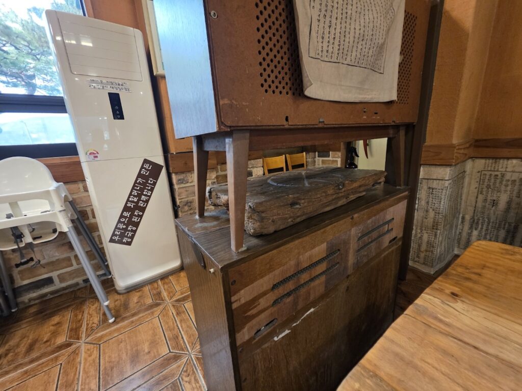 The interior of a traditional Korean restaurant shown in a what is why how guide explained, featuring old wooden cabinets, traditional patterned wallpaper, and a sign mentioning handmade soybean paste.