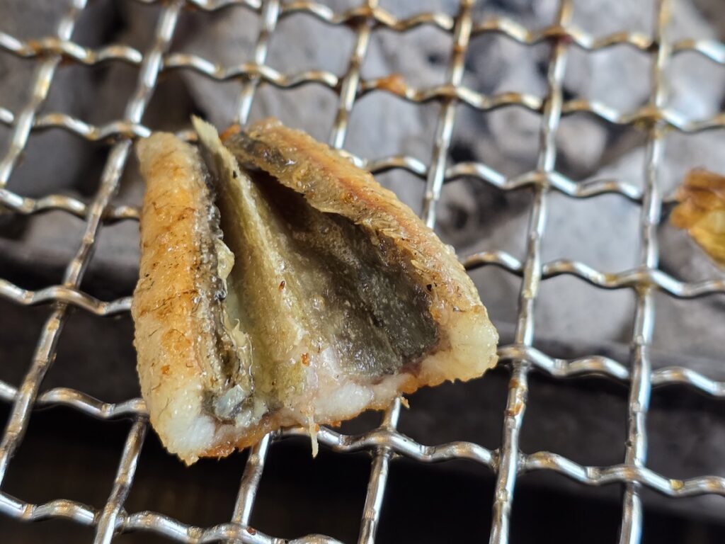 A close-up of a grilled Korean freshwater eel tail on a charcoal grill, symbolizing stamina and health.