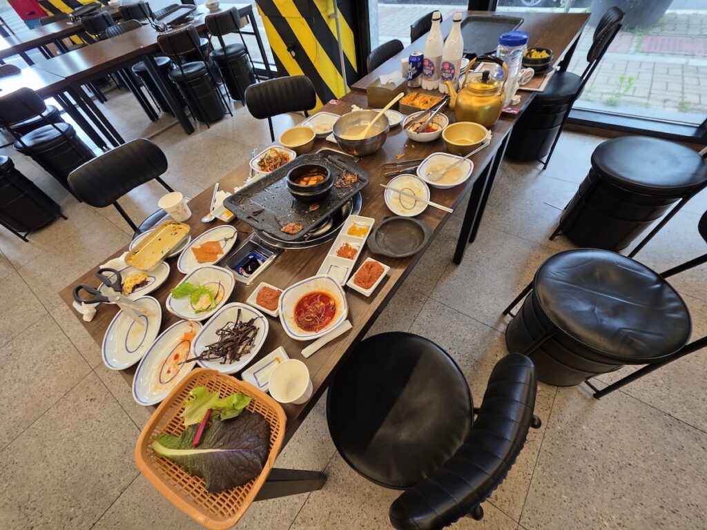 best Korean foods for first time visitors showing samgyeopsal Korean BBQ table after eating with side dishes and grill
