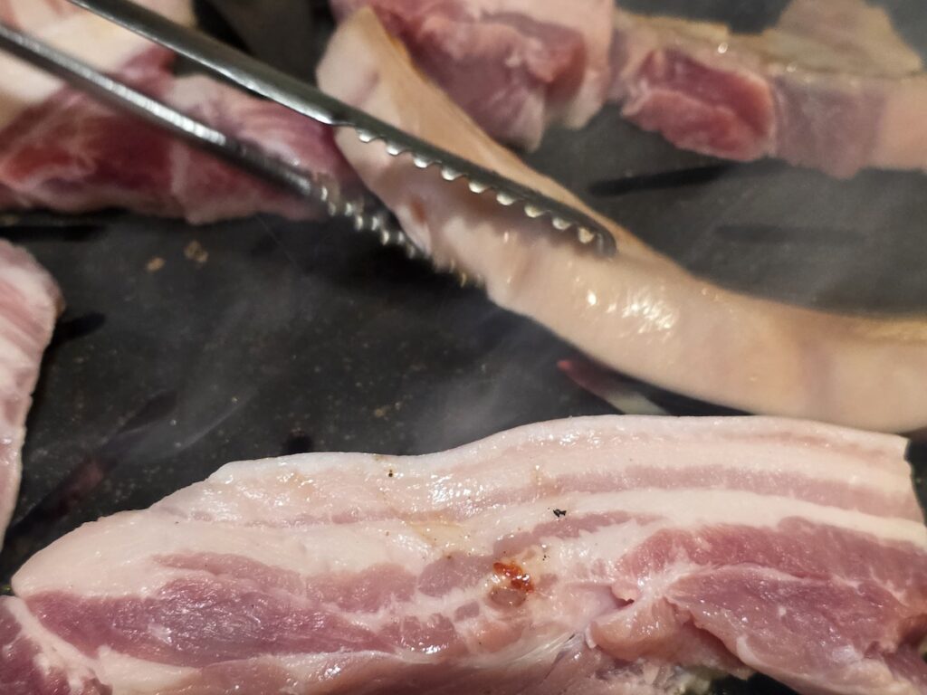 Close-up of raw pork belly showing the distinct layers of fat and meat on a hot grill with smoke rising.