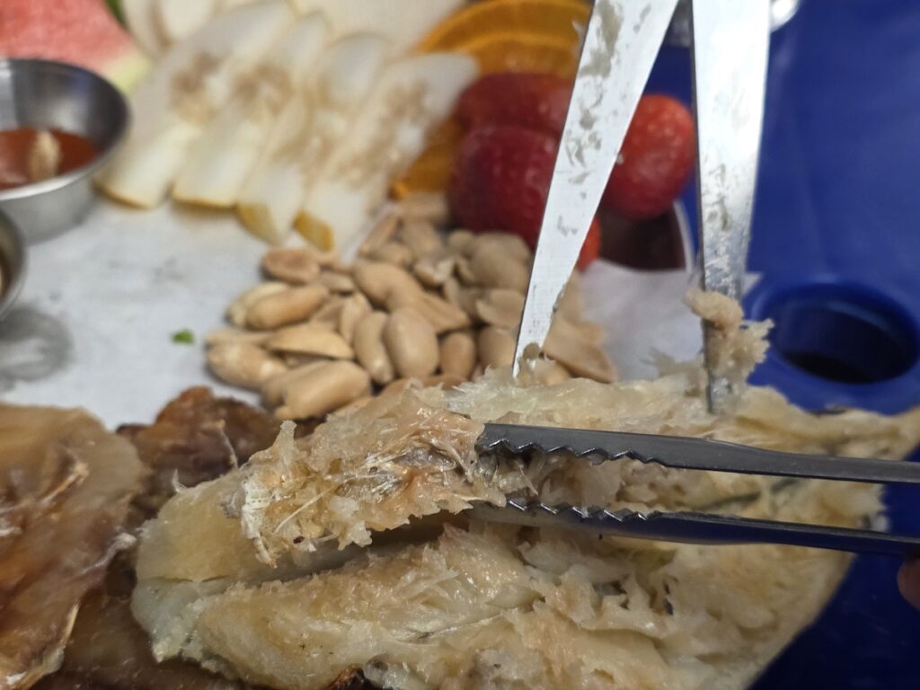 A person using scissors to cut tough, semi-dried young pollack (nogari) served with peanuts as a beer snack.