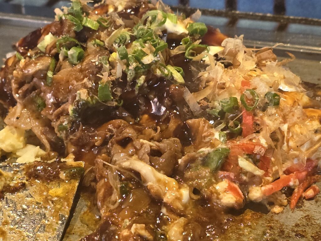 what to eat in Hongdae showing okonomiyaki style dish with sauce and toppings cooked on a hot plate in Seoul
