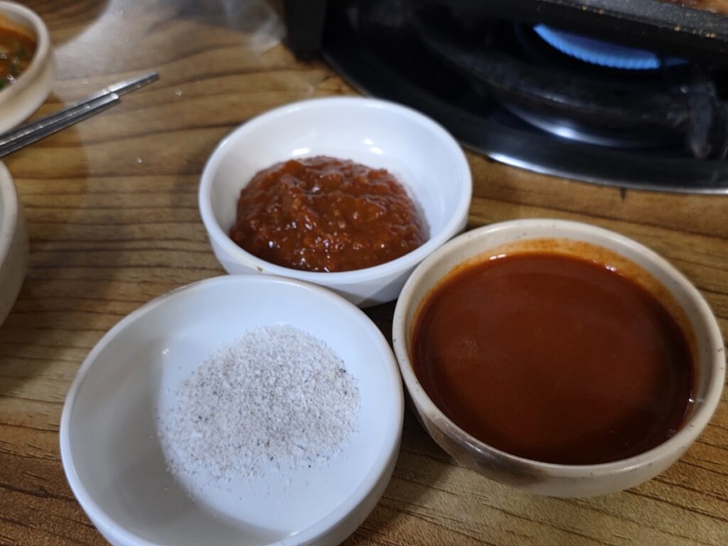 Three small bowls containing different Korean dipping sauces.