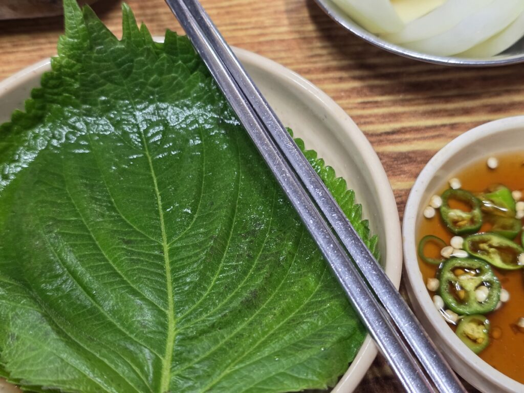 Perilla leaf with chopsticks and green chili soy sauce for wrapping Korean beef intestines gopchang