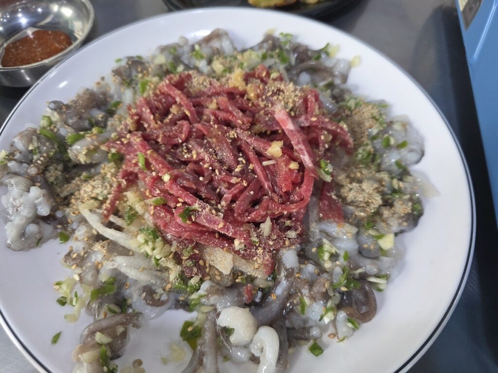 Raw beef and live octopus served on a white plate in Seoul, with yukhoe in the center and chopped octopus around the rim